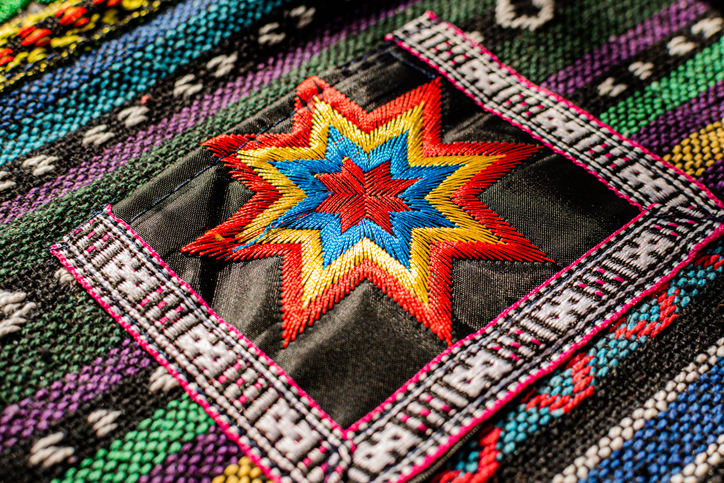 Buntes, geometrisches Stickmuster in Sternform auf gewebtem Stoff.