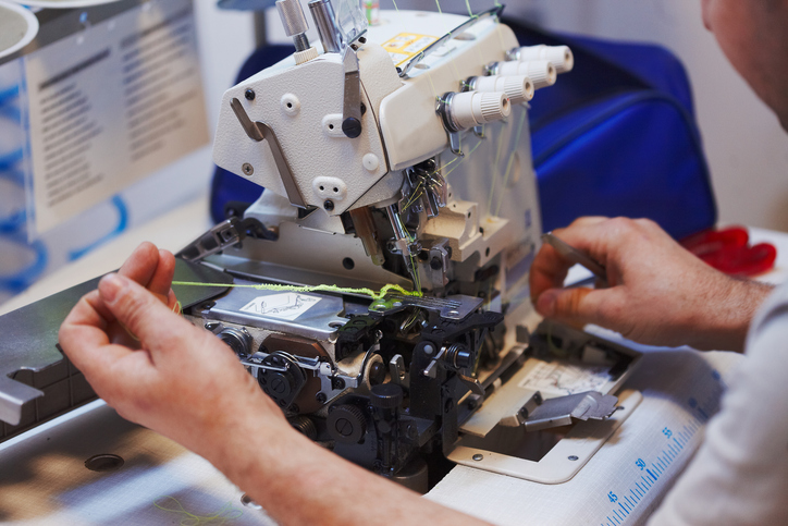 Nahaufnahme einer geöffneten Overlock-Nähmaschine während einer Reparatur oder Wartung, bei der ein Techniker am Nähmechanismus und den Fäden arbeitet.
