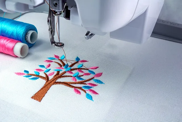 Nähmaschine Ulm - Gestickter Baum mit braunem Baumstamm und bunten Blättern auf einem weißen Stoff