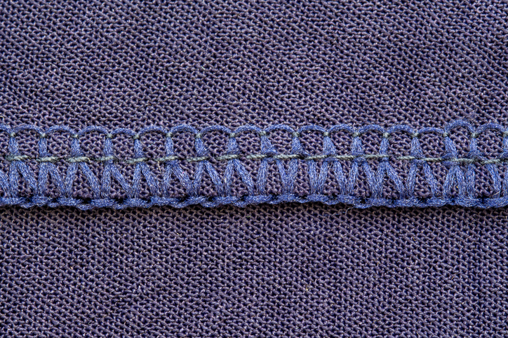 Nahaufnahme einer blauen Overlocknaht, die die Kante eines fein gestrickten Stoffes sauber versäubert.