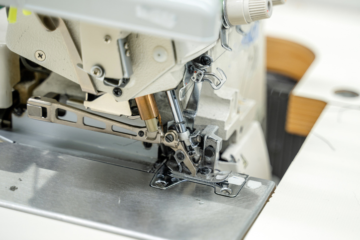 Nahaufnahme des geöffneten Nähbereichs einer Overlock-Nähmaschine mit sichtbaren Nadeln, Nähfuß und mechanischen Bauteilen bei der Wartung.