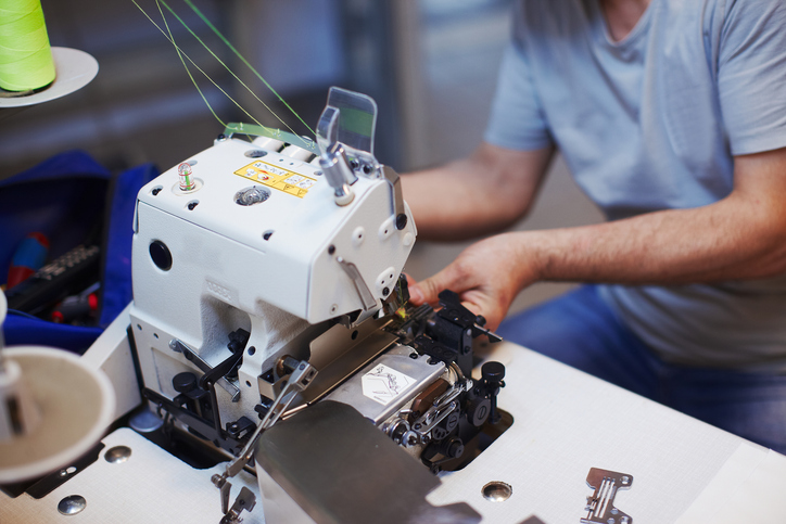 Ein Techniker arbeitet an einer geöffneten Industrienähmaschine mit grünem Garn und führt Wartungs- oder Reparaturarbeiten am Nähmechanismus durch.